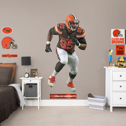 Life-Size Athlete + 12 Decals (41"W x 77"H) Invite Cleveland Browns defensive end Myles Garrett to your personal Dawg Pound with this durable vinyl wall decal. The 2017 first-round draft pick and 2018 Pro Bowl qualifier brings his defensive skills to your bedroom, office, and dog-friendly man cave. Browns Backers will appreciate the classic brown, white, and Cleveland orange, but you don't have to stay in Cleveland. Take this easily reusable decal on the road to wherever life takes you.